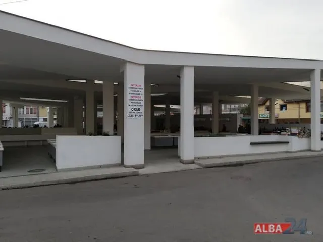 O structură deschisă cu coloane albe susține un acoperiș plat deasupra unor spații comerciale cu mese de prezentare albe.