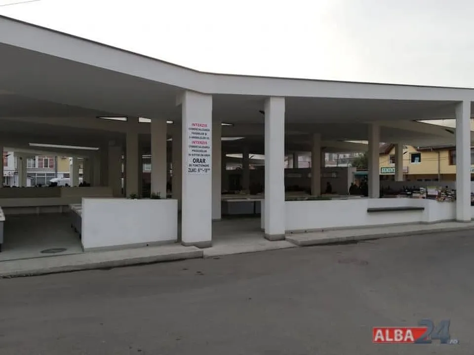 O structură deschisă cu coloane albe susține un acoperiș plat deasupra unor spații comerciale cu mese de prezentare albe.