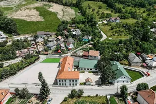 O vedere aeriană prezintă mai multe clădiri cu acoperișuri colorate, drumuri și zone verzi într-un peisaj colinar.
