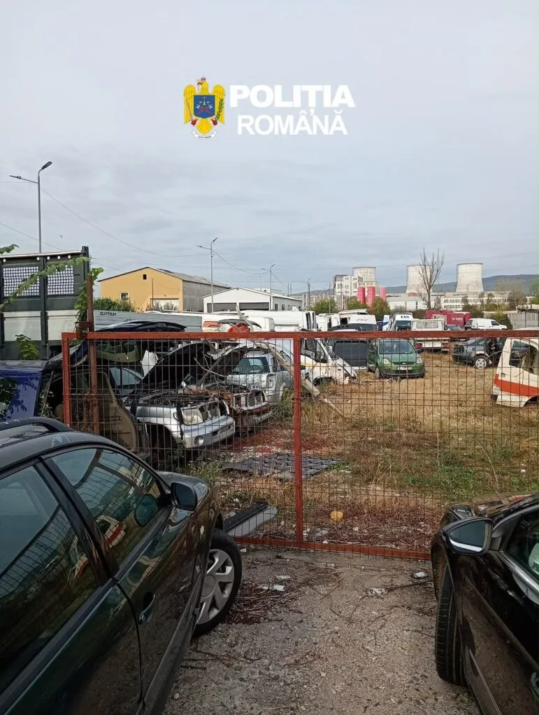 Mai multe vehicule și piese auto sunt depozitate pe un teren cu iarbă și pământ sub un cer înnorat.