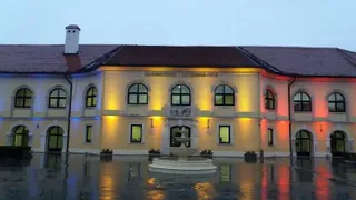 O clădire galbenă cu acoperiș înclinat este iluminată cu lumini colorate pe o suprafață umedă sub un cer închis la culoare.