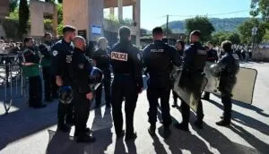Mai mulți polițiști în uniforme închise stau cu spatele într-un grup pe o stradă lângă un vehicul și un scut de protecție.