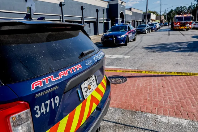 Partea din spate a unui vehicul de poliție albastru cu inscripția Atlanta este parcată pe o stradă lângă un trotuar din cărămidă roșie.