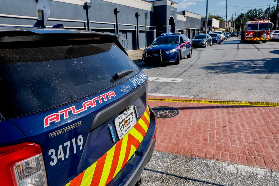 Partea din spate a unui vehicul de poliție albastru cu inscripția Atlanta este parcată pe o stradă lângă un trotuar din cărămidă roșie.