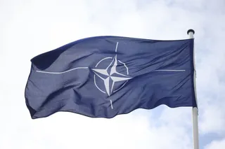 Un steag albastru cu un simbol alb de busolă flutură pe un stârp sub un cer înnorat.