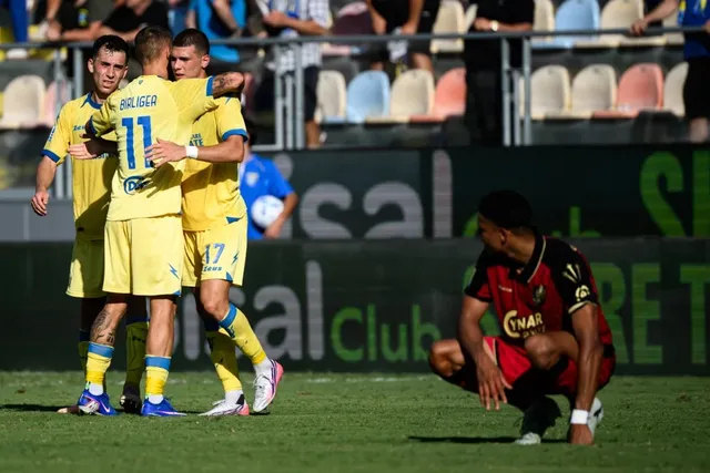 Trei jucători de fotbal în echipament galben se îmbrățișează pe teren, în timp ce un jucător în echipament roșu și negru stă ghemuit pe iarbă.
