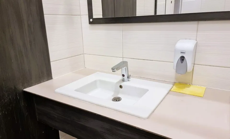 Un chiuvetă albă cu un robinet metalic este montată pe un blat de culoare deschisă lângă un dozator de săpun alb.