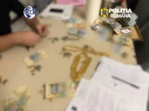 Mânile unei persoane stau deasupra unei mese pe care se află bancnote, documente și un obiect metalic de culoare aurie.