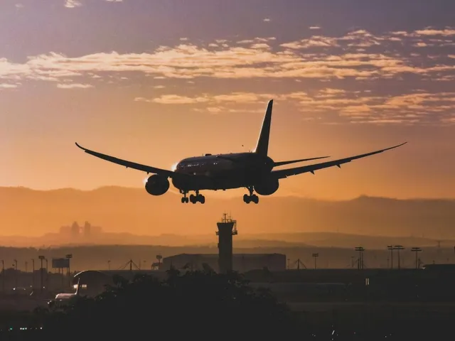 Un avion de pasageri este siluetat în zbor pe un cer la apus, deasupra unei turnițe de control de aeroport.