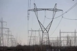 Mai multe turnuri de înaltă tensiune metalice susțin cabluri electrice sub un cer de seară.