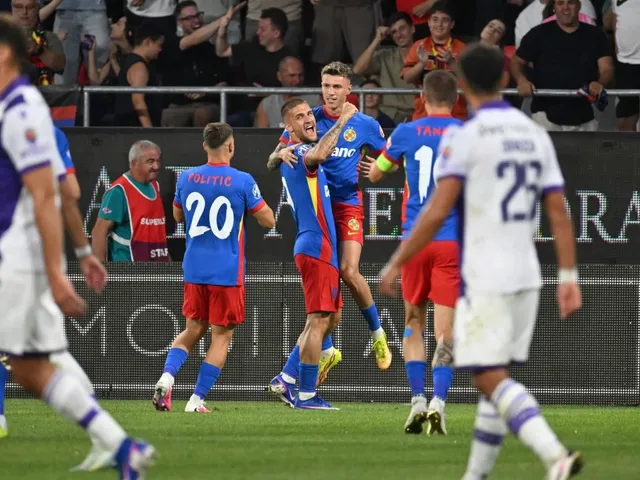Câțiva fotbaliști în echipamente albastre și roșii sărbătoresc pe un teren de fotbal în fața unor spectatori din tribune.