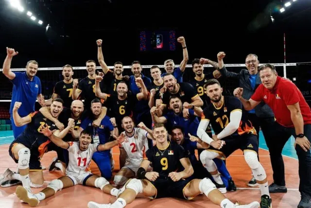 Un grup de sportivi în echipamente de volei negre și albe pozează într-o sală de sport cu brațele ridicate.