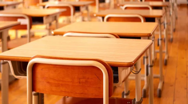 Rânduri de bănci din lemn cu picioare metalice albe dispuse într-o sală de clasă cu podea de lemn.