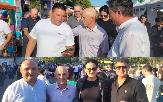 Un grup de persoane stă în picioare afară, în timp ce unii privesc spre un telefon mobil.