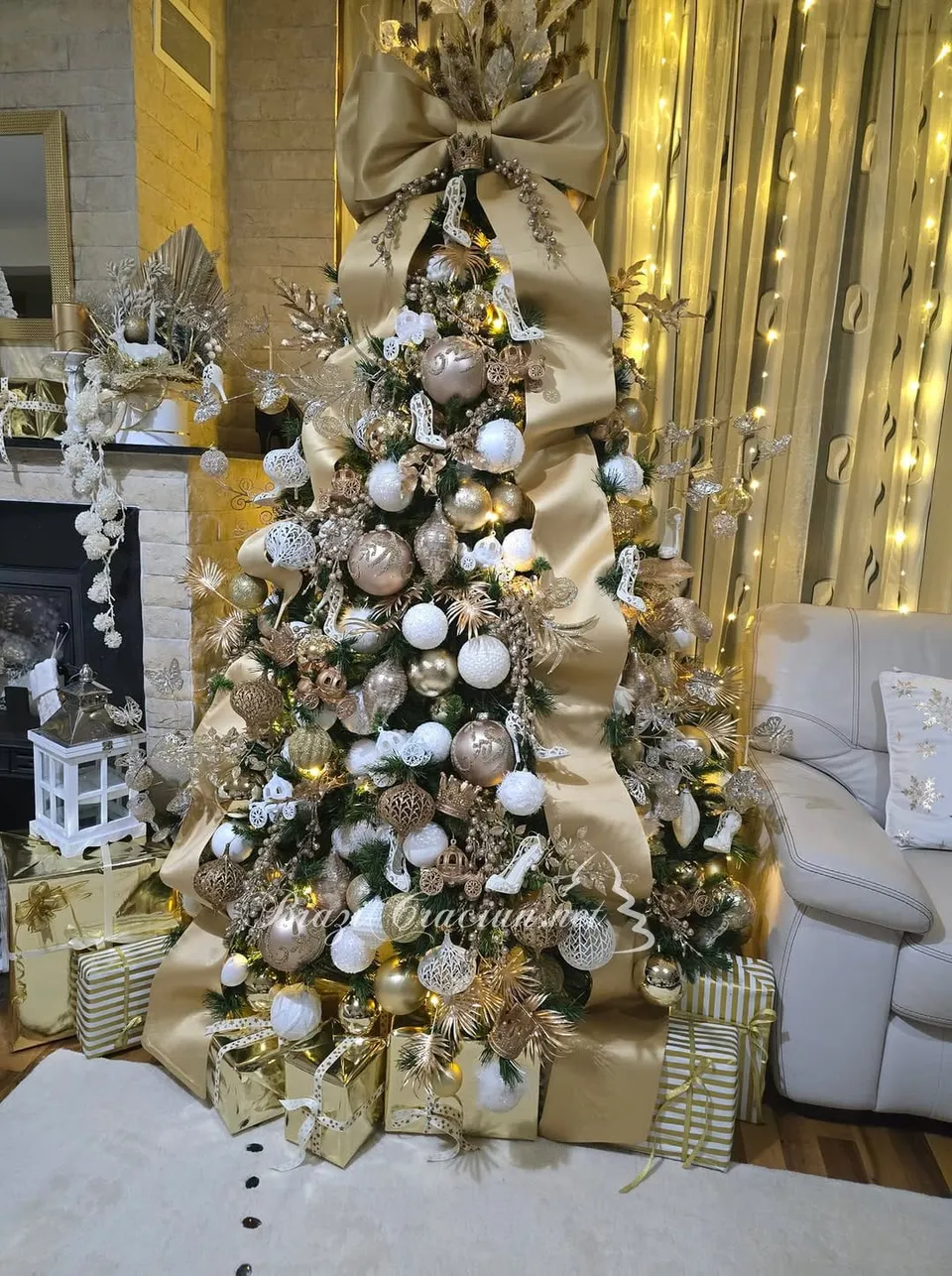 Un brad de Crăciun decorat cu decorațiuni aurii și albe, ornate cu o panglică mare și cutii de cadouri la baza acestuia.
