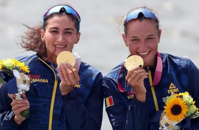 Două femei zâmbesc purtând jachete sport, medalii aurii și buchete de flori.