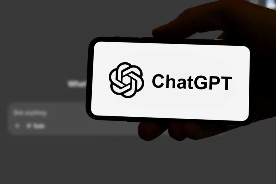 O mână ține un smartphone care afișează logo-ul și textul ChatGPT pe un ecran alb.