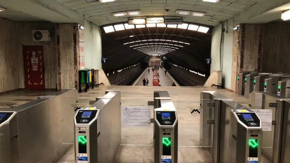 Rând de turnिकete metalice cu ecrane digitale și lumini verzi este poziționat în fața unui tunel de metrou cu lumină artificială.