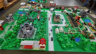 O dioramă construită din piese LEGO prezintă clădiri, vegetație verde, trenuri și vehicule pe o suprafață plană de prezentare.