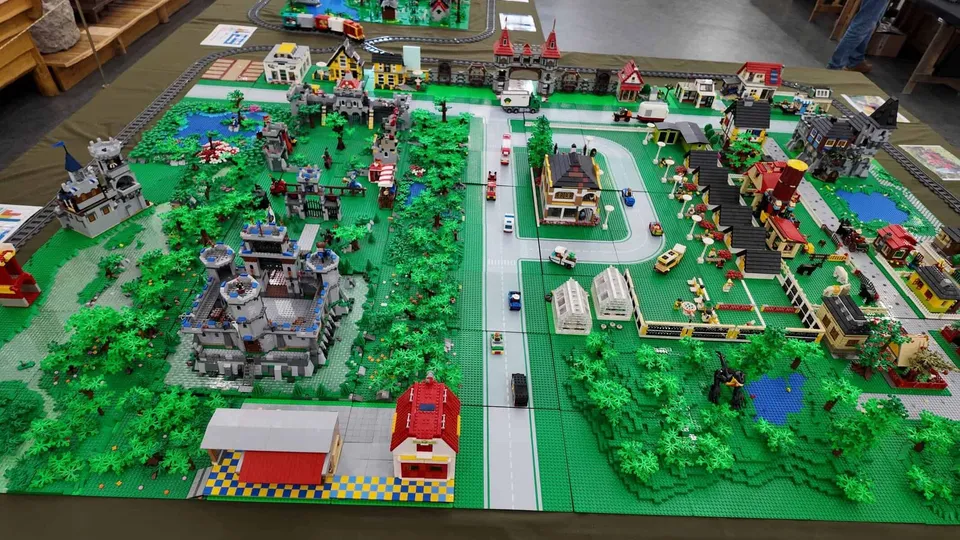 O dioramă construită din piese LEGO prezintă clădiri, vegetație verde, trenuri și vehicule pe o suprafață plană de prezentare.