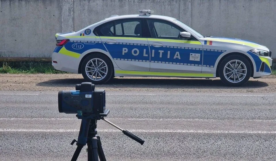 O mașină de poliție albă și albastră cu inscripția POLITIA este parcată pe un drum lângă un aparat de măsurare montat pe un trepied.