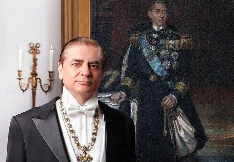 Un bărbat cu frac, papion alb și un colier decorativ stă în fața unui tablou reprezentând un oficial în uniformă militară.