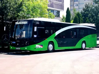 Un autobuz negru și verde cu inscripția Primaria Brasov este parcat pe un drum lângă copaci verzi.
