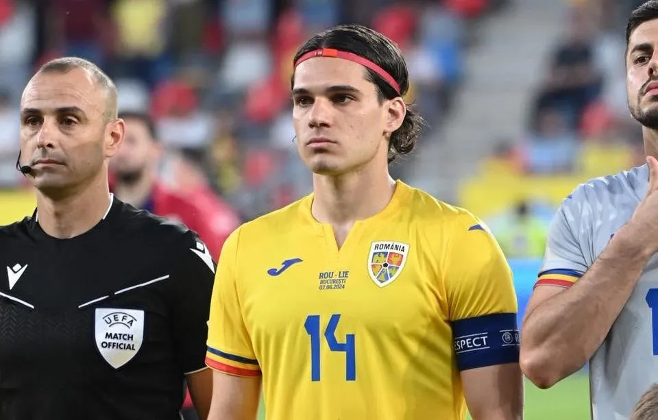 Un bărbat cu o bandană roșie și un tricou galben cu numărul 14 stă lângă un arbitru îmbrăcat în negru.