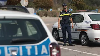 Un polițist stă în picioare lângă o mașină de poliție albă pe un drum asfaltat.