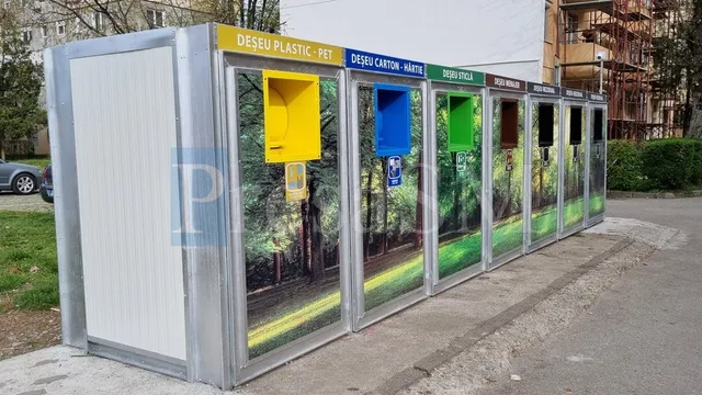 O serie de containere metalice colorate pentru colectarea deșeurilor este aliniată pe un trotuar lângă un drum asfaltat.