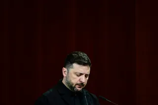 Un bărbat cu barbă și păr scurt, îmbrăcat în haine negre, stă cu privirea în jos în fața unui microfon.