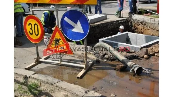 Un șantier cu semne de circulație, un șanț deschis și o conductă de pe o stradă cu apă pe jos.