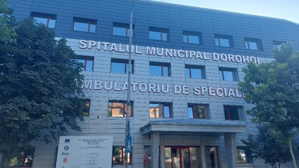 O clădire cu fațadă gri și ferestre rectangulare prezintă inscripții pe perete și un panou informativ alb în partea stângă jos.