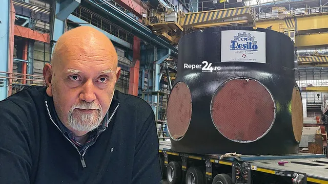 Un bărbat cu barbă și păr scurt de culoare deschisă stă în prim-plan, în timp ce în fundal se află un obiect metalic cilindric pe un trailer.