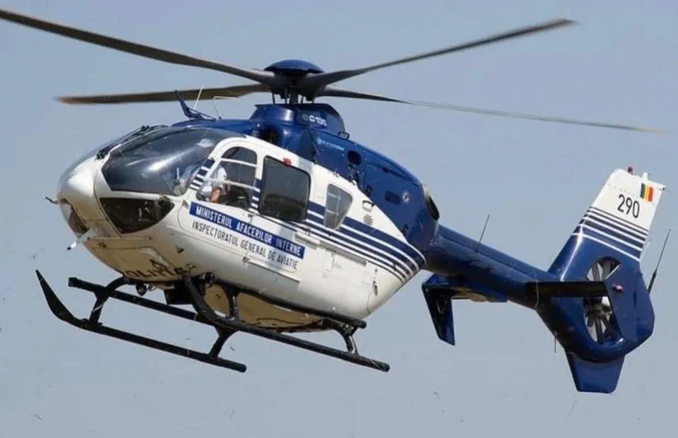 Un elicopter albastru și alb cu marcaje pe fuselaj zboară pe un cer senin.