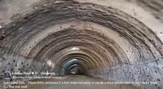 O galerie de tunel cu pereți și tavan curbați, acoperiți cu un strat de beton gri și elemente metalice dispuse periodic.