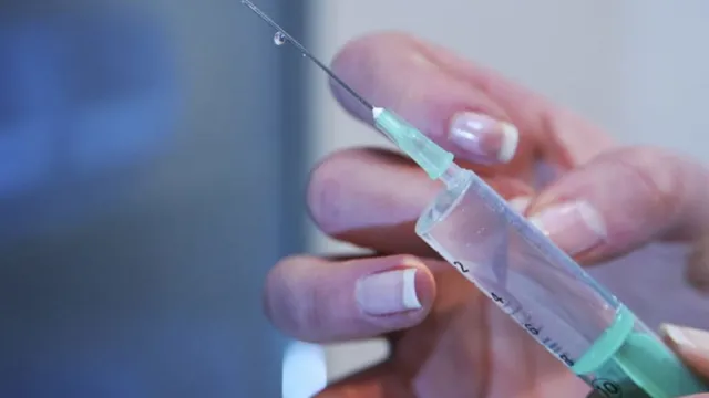 O persoană cu unghii pictate ține o seringă cu un ac subțire, pregătită pentru injectare.
