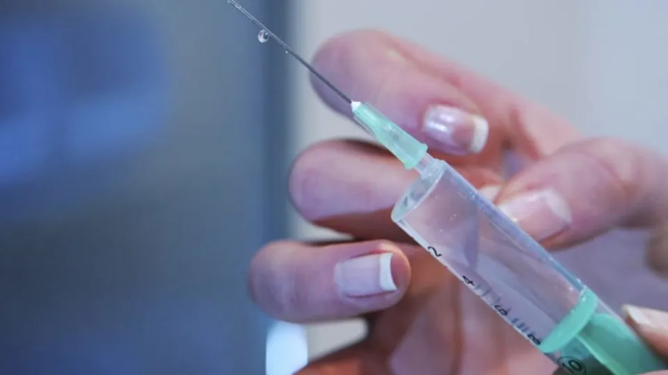 O persoană cu unghii pictate ține o seringă cu un ac subțire, pregătită pentru injectare.