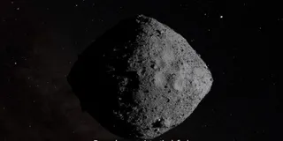 Un asteroid de formă neregulară și suprafață craterată este vizibil pe un fundal negru presărat cu puncte luminoase mici.