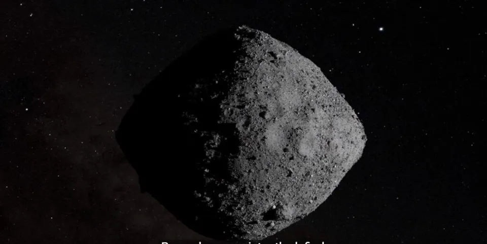 Un asteroid de formă neregulară și suprafață craterată este vizibil pe un fundal negru presărat cu puncte luminoase mici.