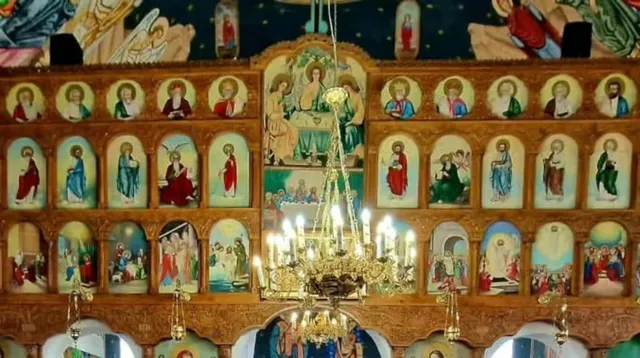 Un iconostas din lemn cu numeroase picturi religioase de tip icoană dispuse în mai multe rânduri, sub un candelabru metalic suspendat.