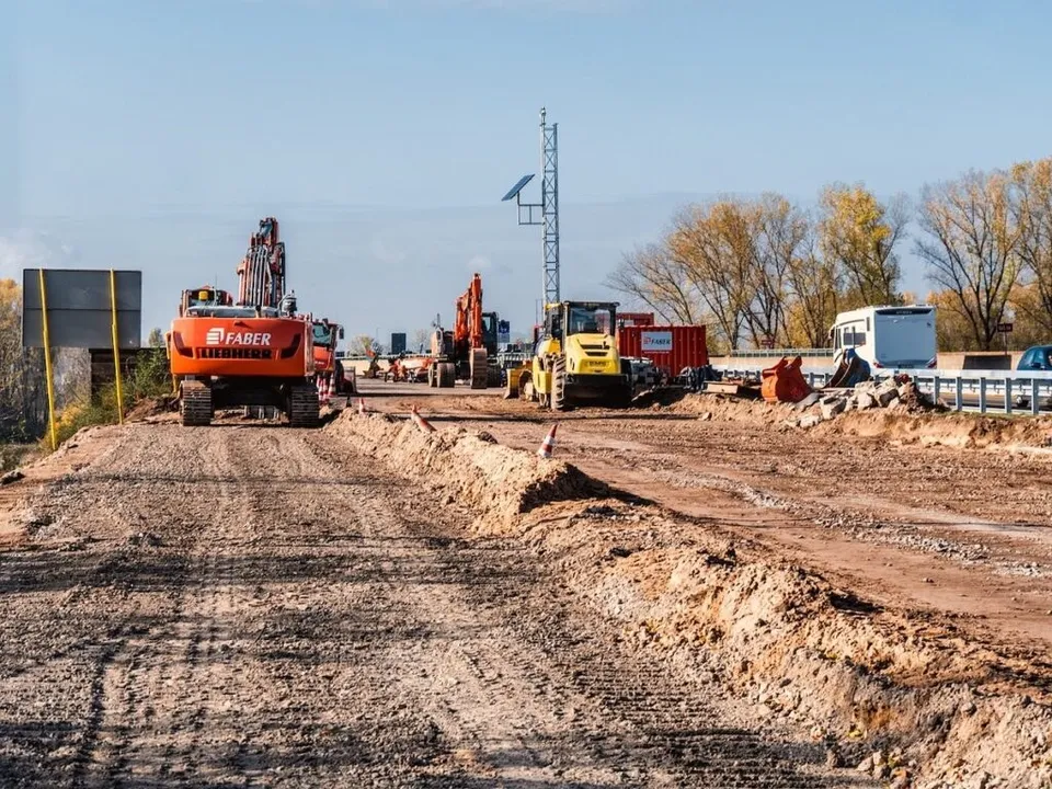 Mașini de construcții și utilaje de excavare sunt poziționate pe un teren de pământ întins sub un cer senin.