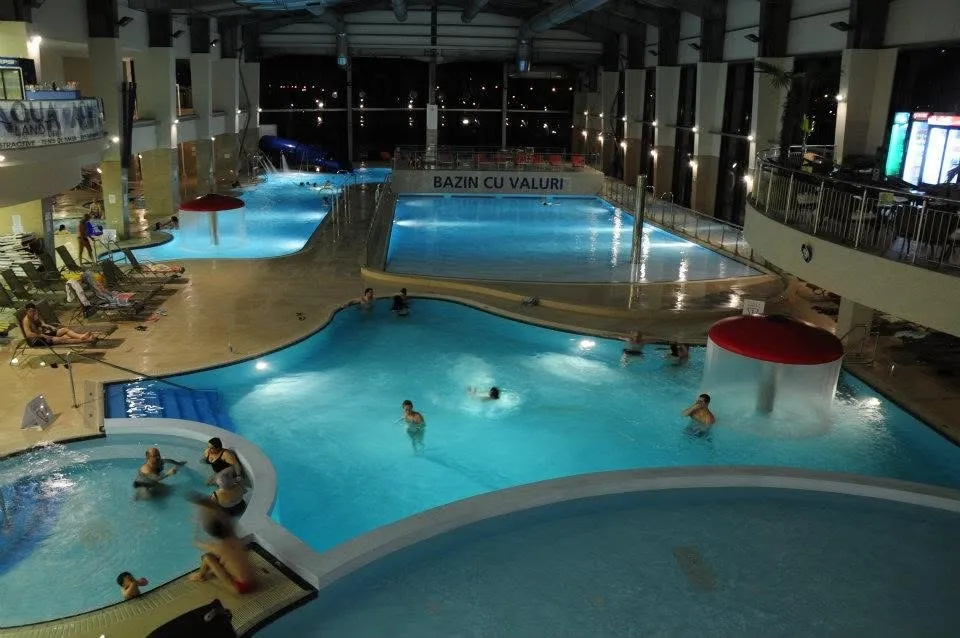 O vedere de sus asupra mai multor piscine interioare cu oameni care înoată și șezând pe marginea apelor albastre.