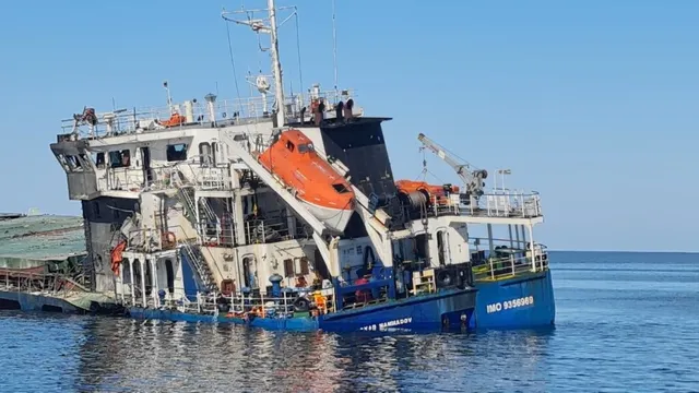 O ambarcațiune albastră și albă cu un salvamarport de culoare portocalie este plutind pe apă sub un cer senin.