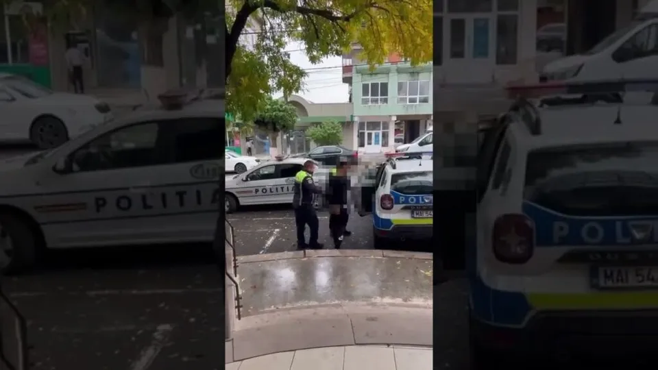 Două mașini de poliție și un vehicul alb sunt parcate pe o stradă lângă un grup de trei persoane.