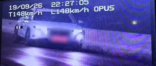 O mașină albă circulă pe un drum noaptea, fiind surprinsă de o cameră de monitorizare care afișează date textuale pe ecran.