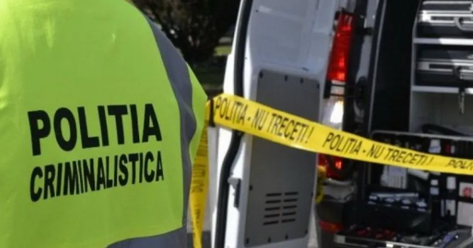 Un membru al poliției cu vestă reflectorizantă stă lângă spatele unui vehicul alb marcat cu o bandă galbenă de poliție.