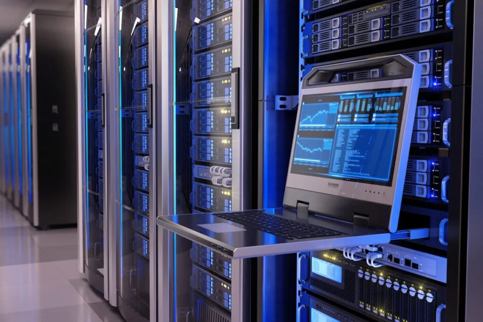 Rânduri de rack-uri de servere cu lumini albastre sunt situate într-o cameră, lângă un monitor de control cu grafice afișate pe ecran.