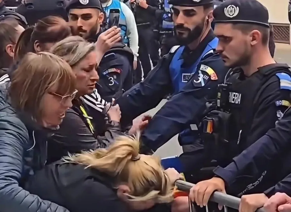 Mai mulți agenți în uniformă albastră și neagră interacționează cu un grup de persoane într-un spațiu public aglomerat.