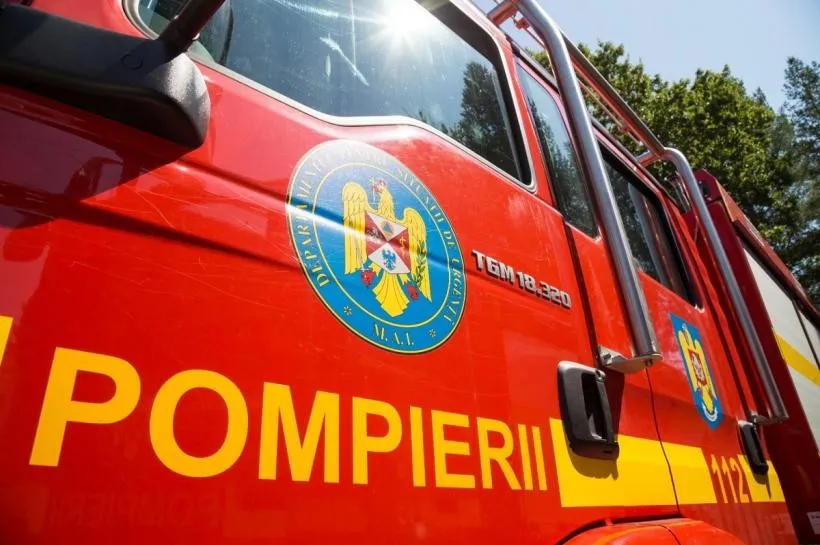 Un vehicul de serviciu de culoare roșie prezintă inscripția POMPIERII și un emblem circular pe lateralul său.
